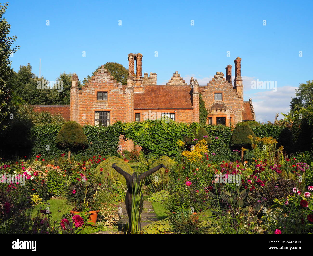 Chenies Manor House sur une soirée de fin d'été, jardin en contrebas dahlias, chemins d'herbe et de plantes border.bassin d'agrément avec statue d'atteindre le haut. Banque D'Images