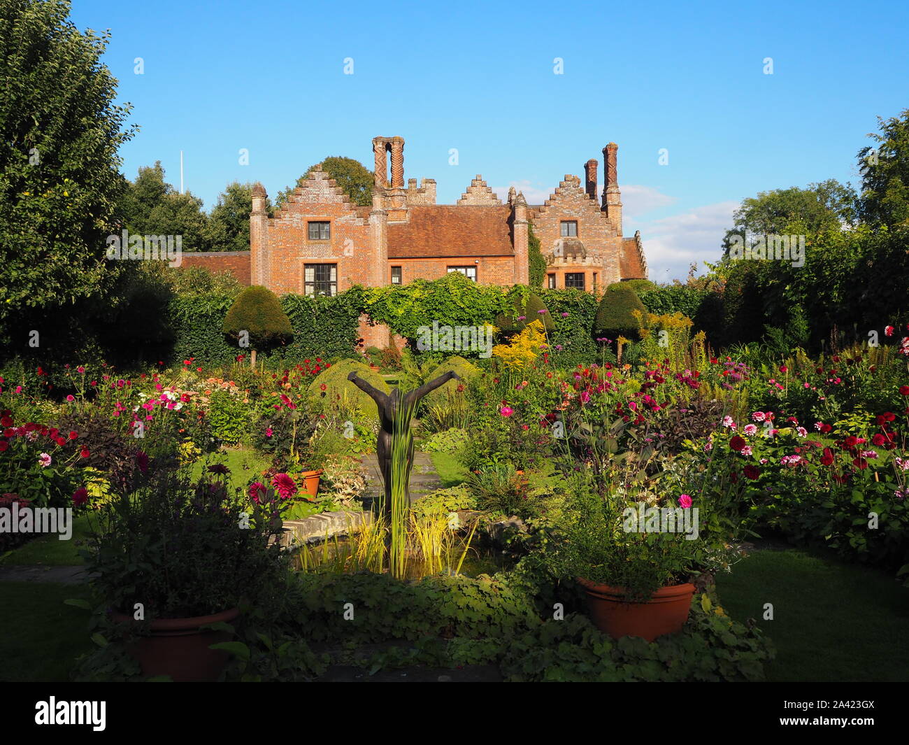 Chenies Manor House sur une soirée de fin d'été, jardin en contrebas dahlias, chemins d'herbe et de plantes border.bassin d'agrément avec statue d'atteindre le haut. Banque D'Images