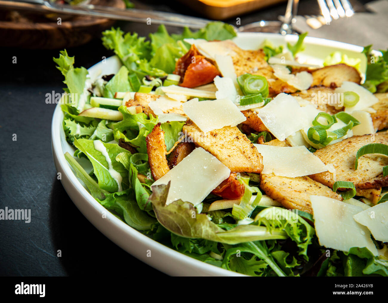 Salade de poulet grillé et de létuques mélangées avec oignons verts, copeaux de parmesan, assaisonnés avec sauce à l'ail, Banque D'Images