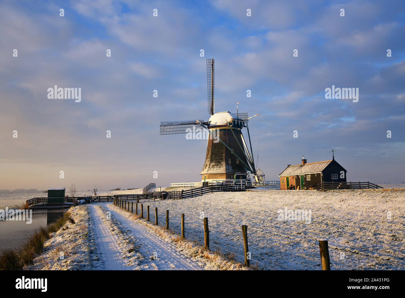 Un moulin à vent et une maison sous la neige au soleil du lever du soleil un jour d'hiver dans un paysage dans la campagne hollandaise aux Pays-Bas. Banque D'Images