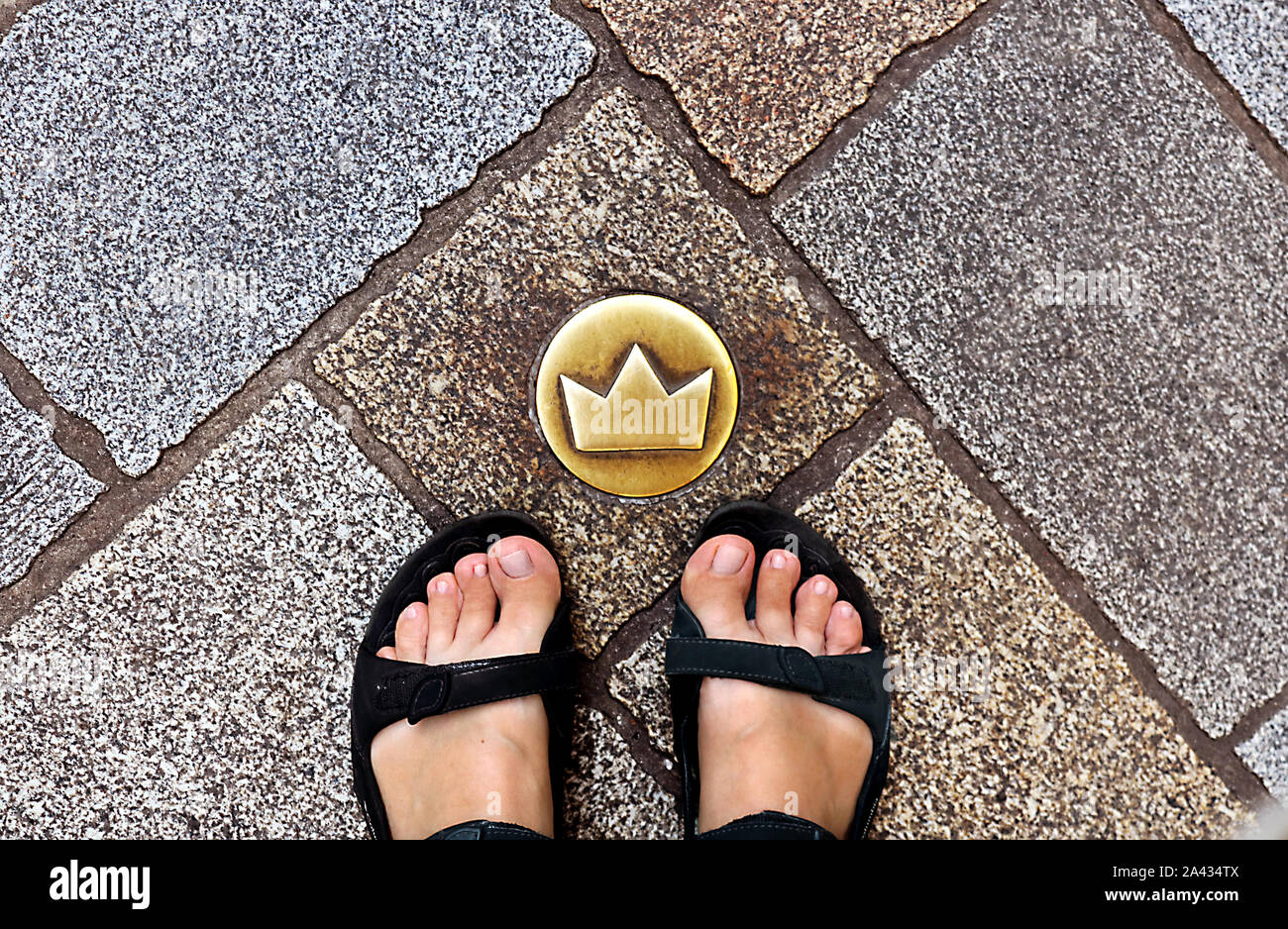 Vue de dessus du touriste fatigué les jambes en sandales et couronne en laiton marqueur dans des rues pavées qui indique l'emplacement du couronnement de marche, Bratislava, République Slovaque Banque D'Images