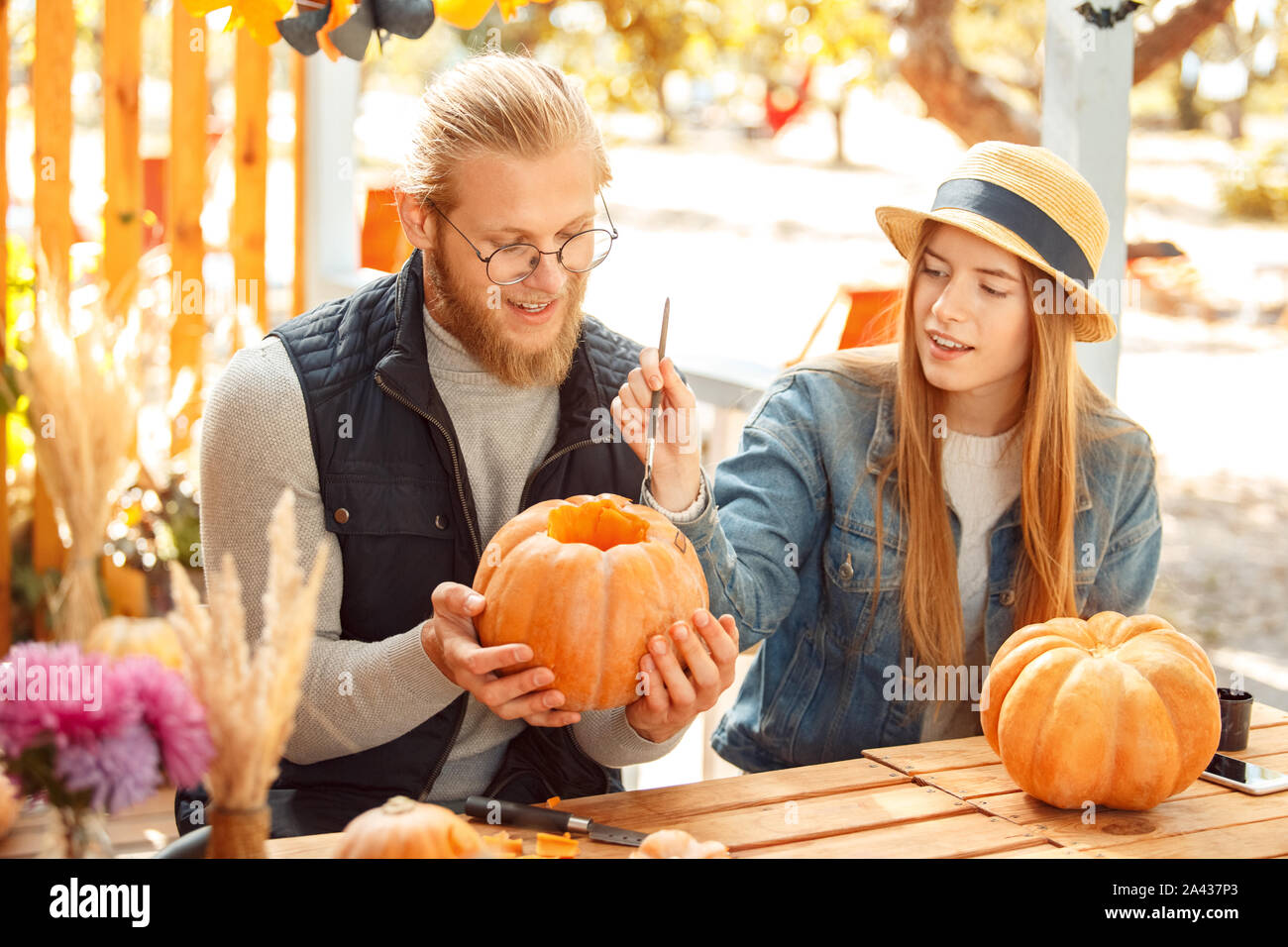 Preparaton Halloween Concept. Jeune couple assis à table à l'extérieur faire jack-o'-lantern citrouille peinture sur visage souriant inspiré Banque D'Images