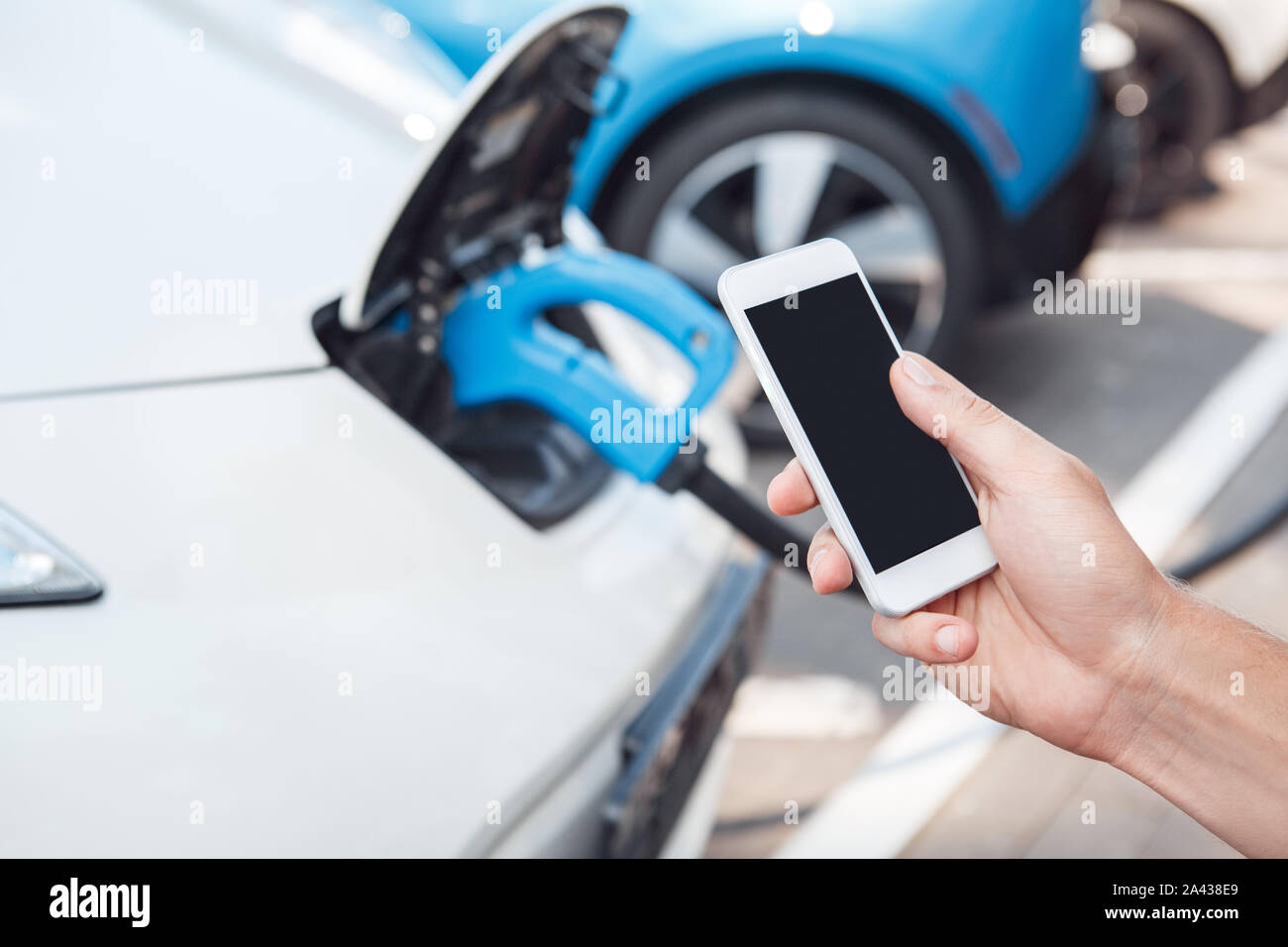 Young adult man using smartphone et de payer pour la voiture électrique de charge Banque D'Images