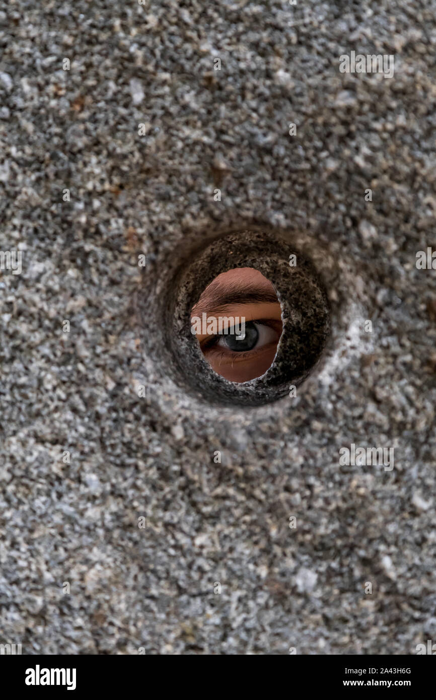 Oeil ouvert à la recherche à travers le trou rond dans mur de pierre Banque D'Images