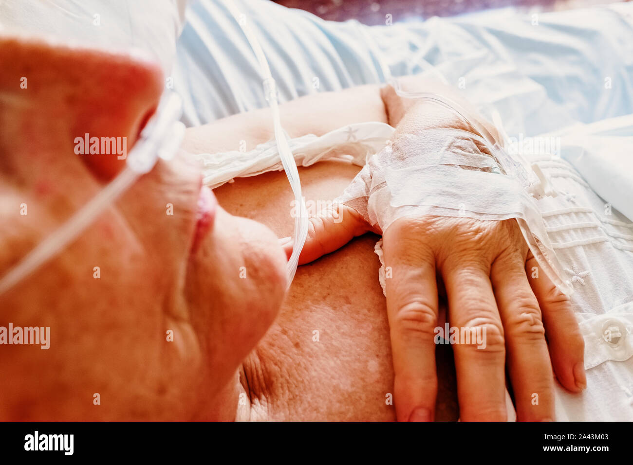 Détail d'un patient de respirer de l'oxygène au moyen d'une canule nasale en plastique et d'une canule intraveineuse insérée dans la main. Banque D'Images