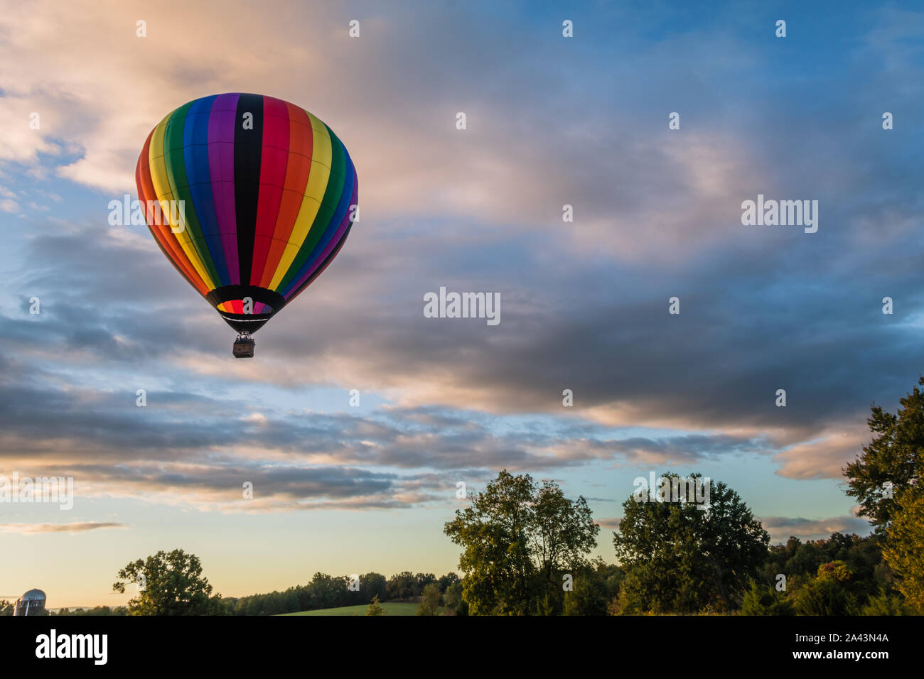 Montgolfière arc-en-ciel flotte au-dessus au lever du soleil sur le terrain Banque D'Images