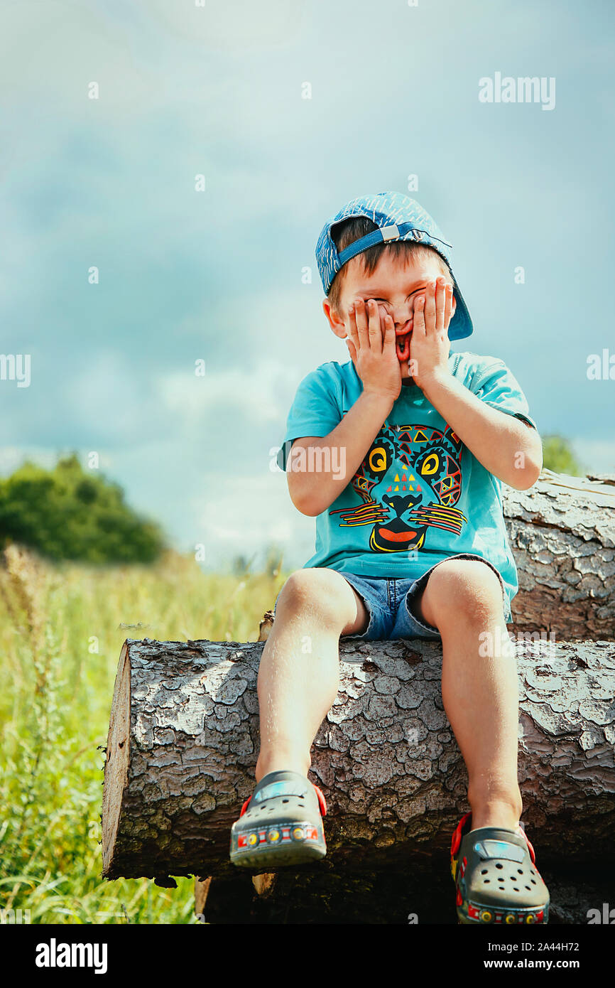 Un garçon d'une casquette bleu et short court se trouve sur un log de jouer  et de tordre son visage Photo Stock - Alamy
