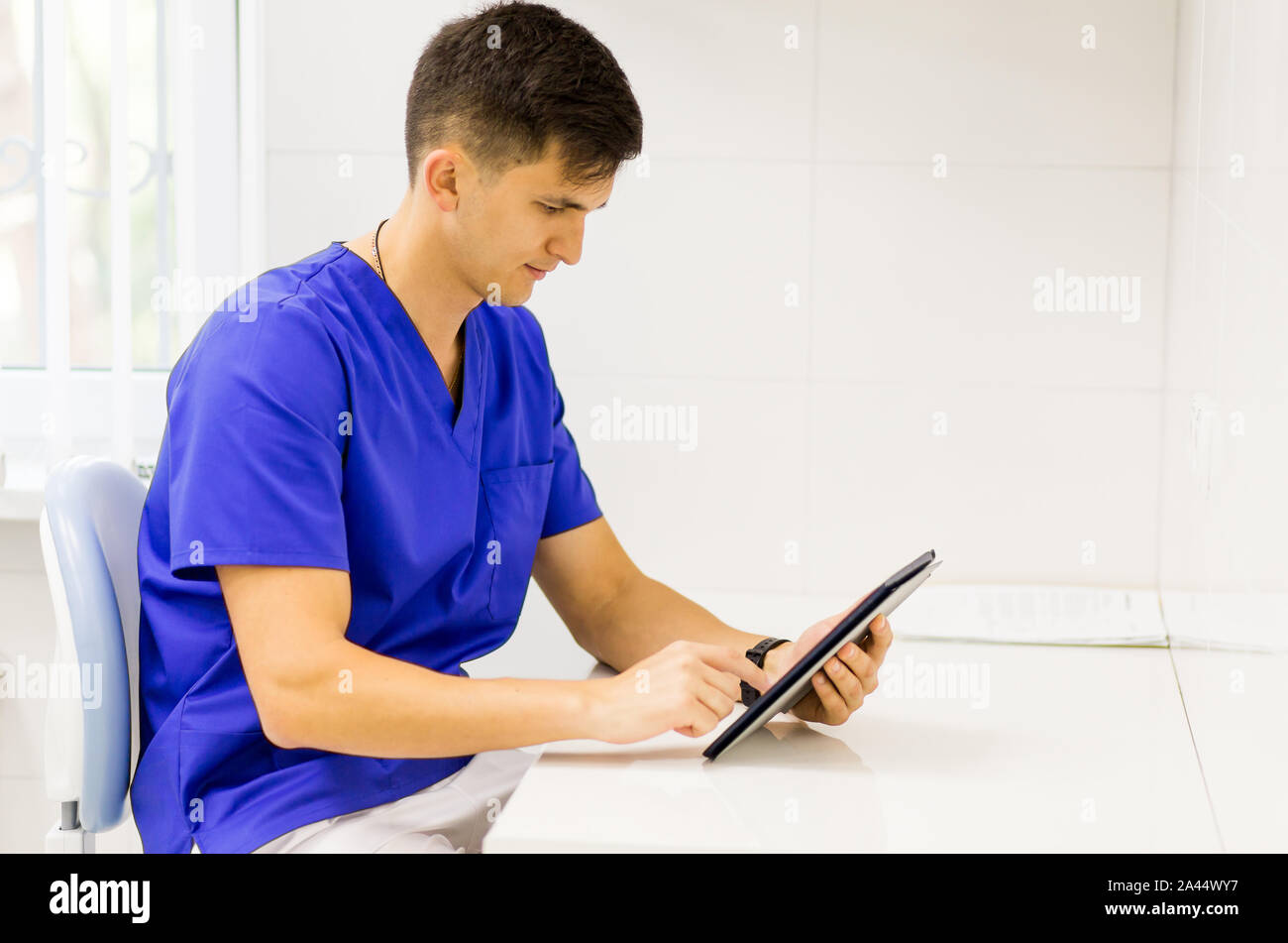 Woman blue coat travaillant sur la ligne avec une tablette dans un dentiste clinique. Banque D'Images