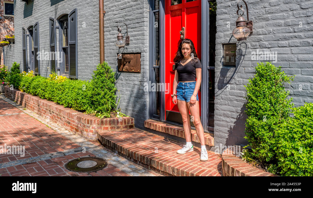 Teen asiatique en short et baskets, debout devant la porte des maisons de briques colorées holding jacket Banque D'Images