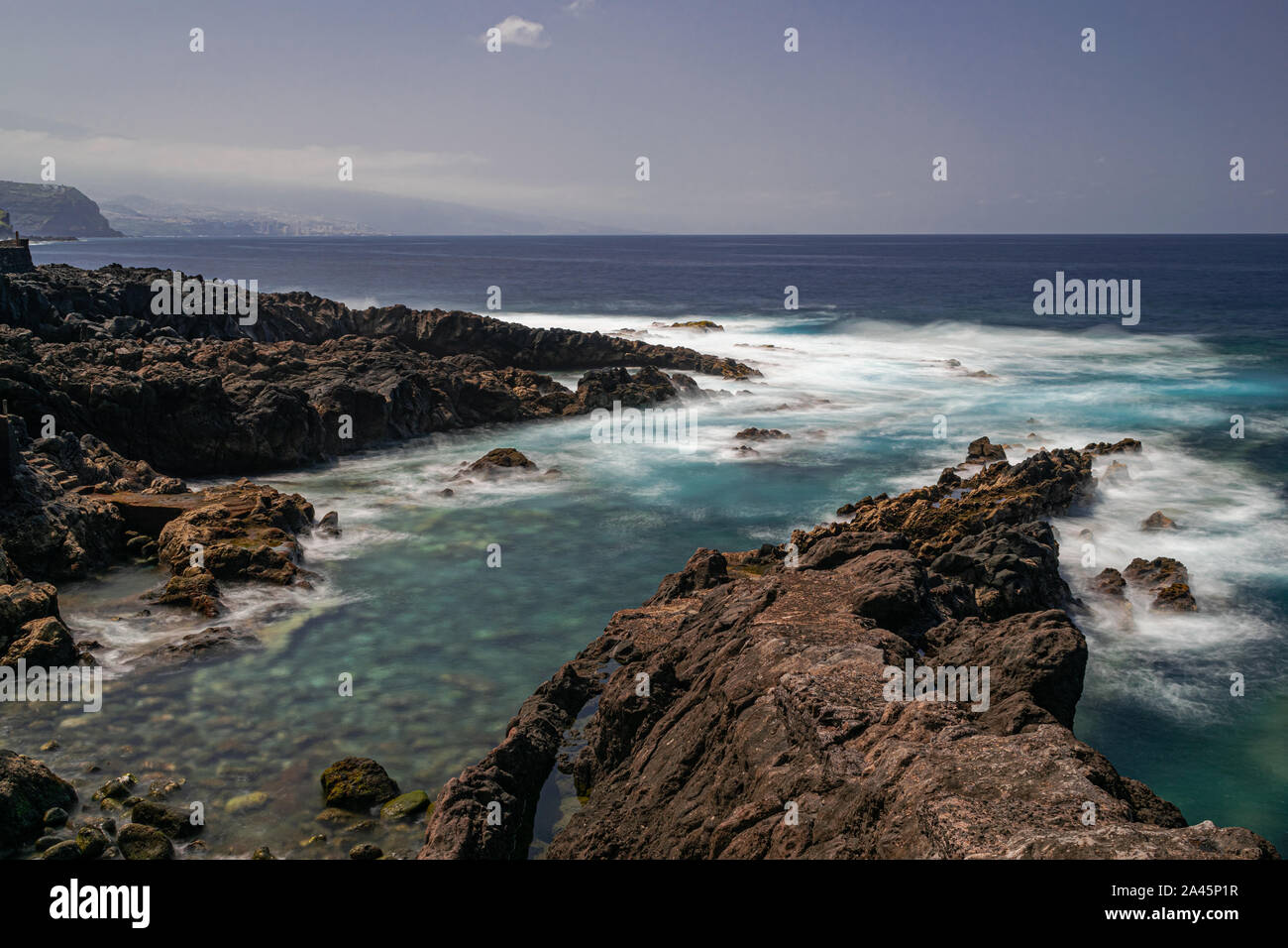 Littoral de roches volcaniques avec la lumière du soleil de l'après-midi, bleu océan Atlantique avec des vagues de mousse, d'une exposition longue, Rojas, El Sauzal, Tenerife, Canaries, Espagne Banque D'Images