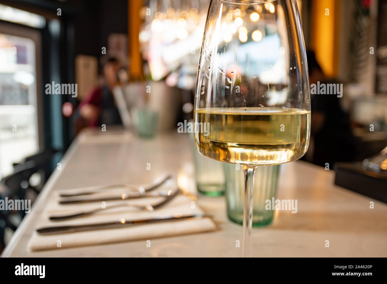Photo d'un comptoir de restaurant avec un gros plan sur un verre de vin blanc et une vue défocuée sur un emplacement moderne en arrière-plan. Banque D'Images