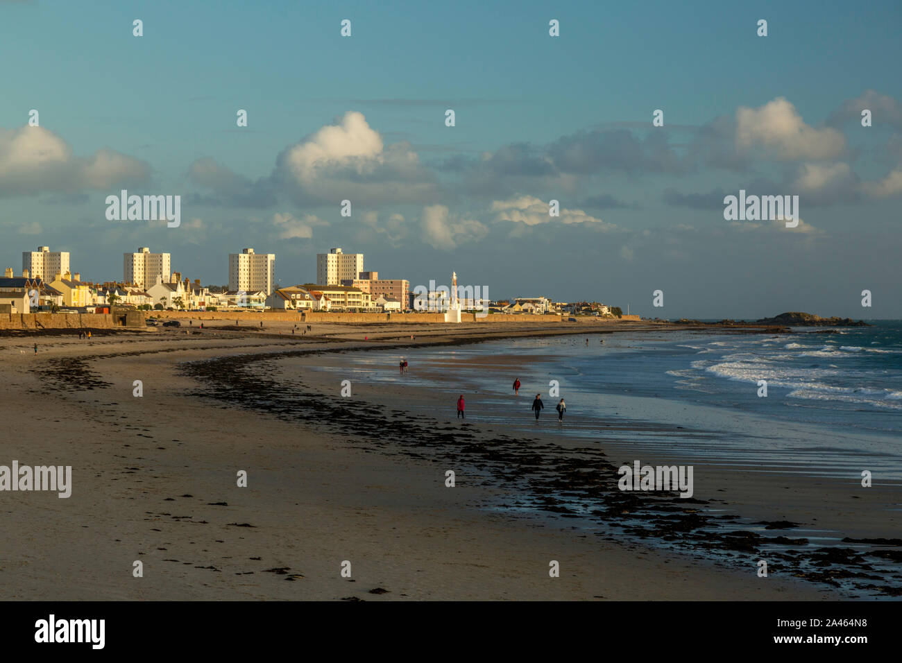 Personnes marchant sur une plage de Jersey dans les îles de la Manche, pendant le coucher du soleil, avec un horizon de hôtels et autres bâtiments en arrière-plan. Banque D'Images