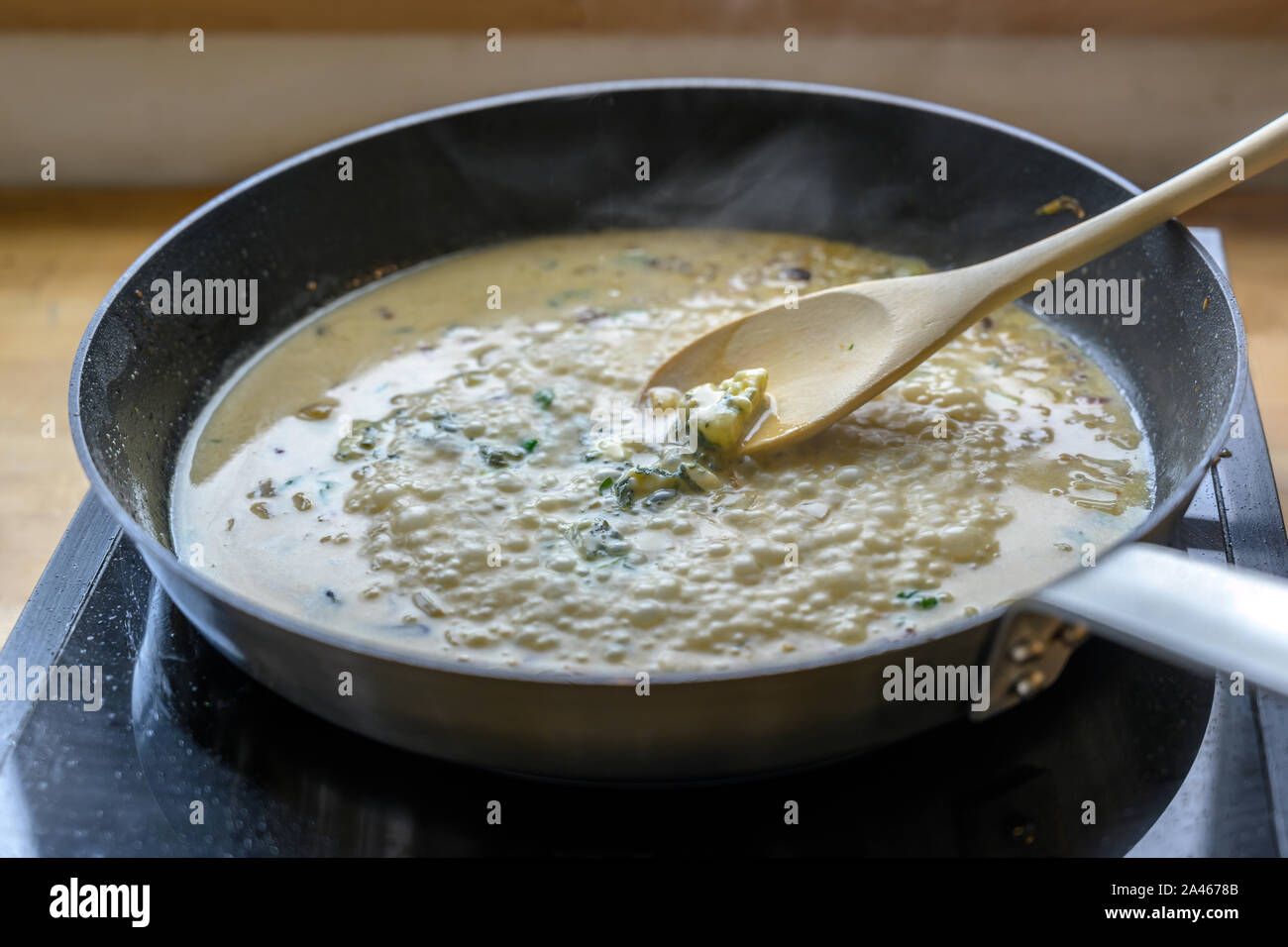 Sauce au fromage gorgonzola ébullition dans la casserole sur un poêle est remué avec une cuillère en bois, concept de cuisine, de discussion, de la profondeur de champ étroite Banque D'Images