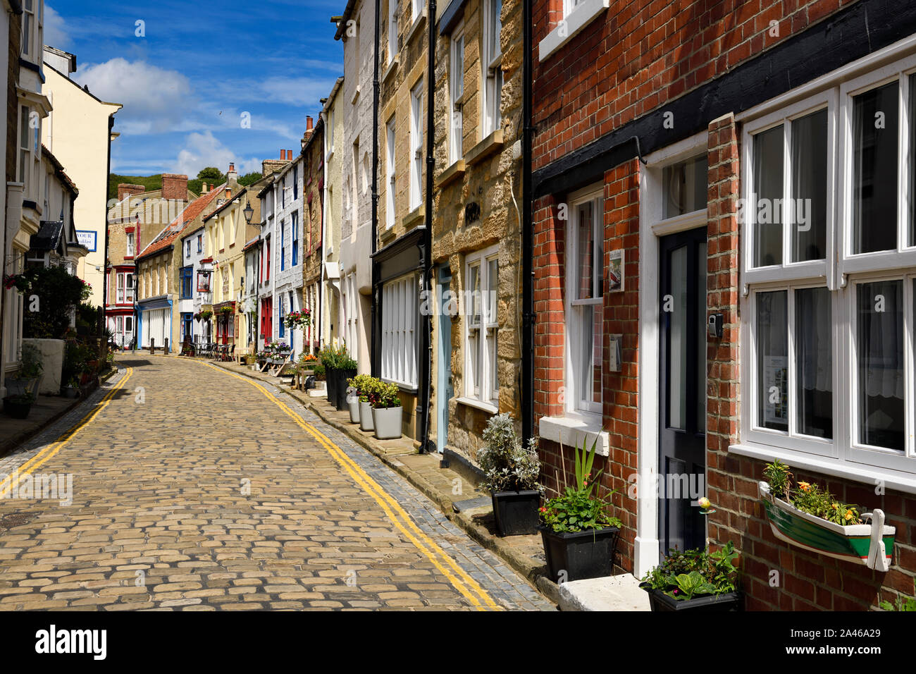 Les plantes en pots et colorée des bâtiments en pierre de soleil sur cobblestone High Street, dans le village balnéaire de Staithes North Yorkshire Angleterre Banque D'Images