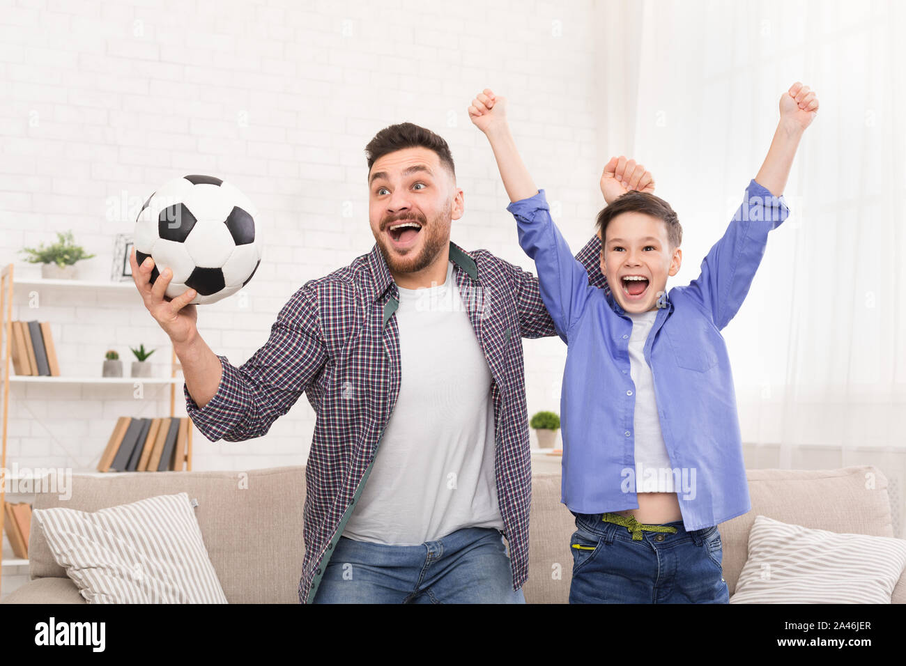 Père et fils émotionnelle avec acclamations, balle de football célèbre but à Accueil Banque D'Images