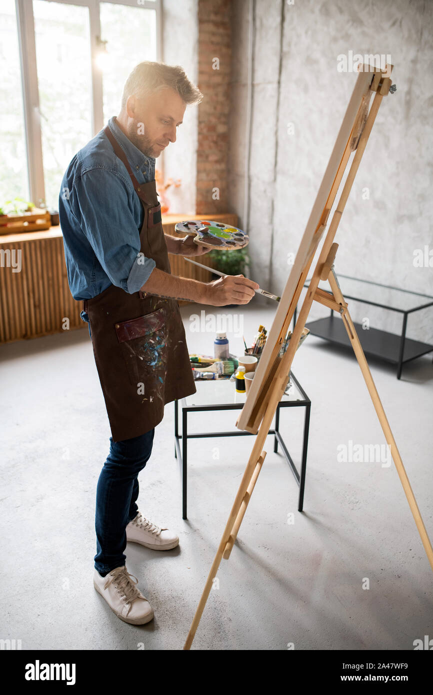 Homme en tablier, debout devant un chevalet et la peinture avec des  couleurs de l'eau Photo Stock - Alamy