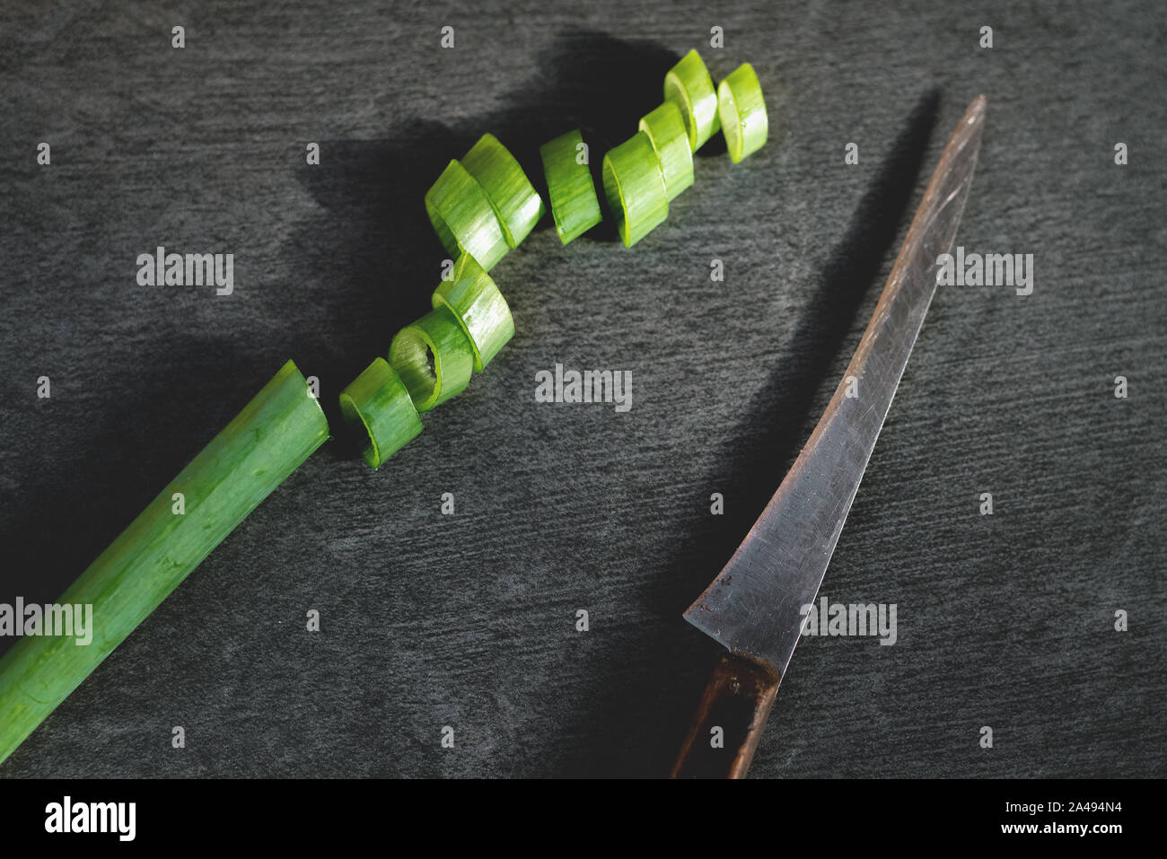 L'oignon et couteau de cuisine sur une planche à découper noire pierre fond. Banque D'Images