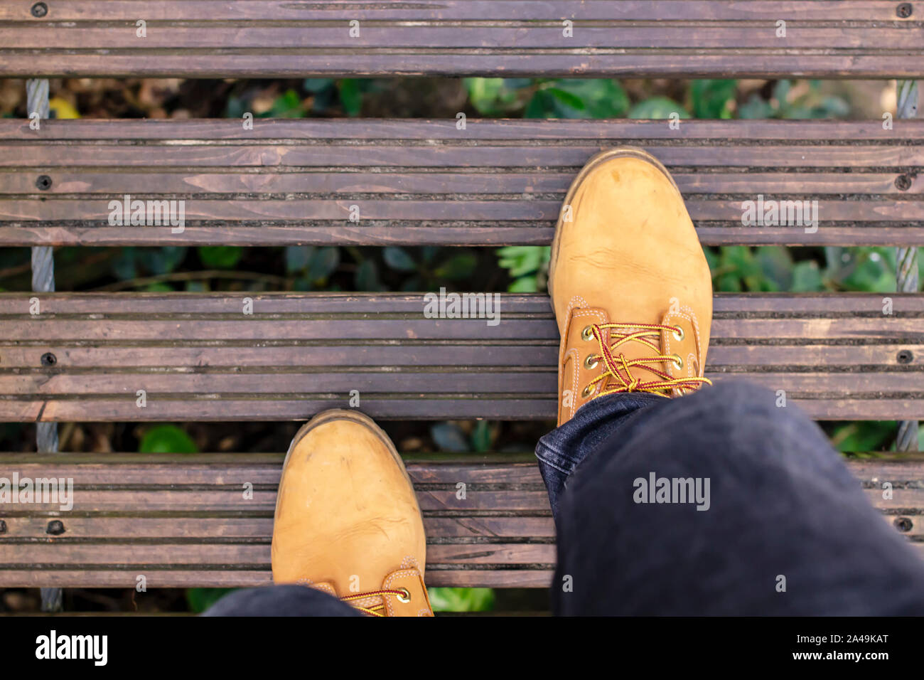 Un homme en jaune promenades bottes avec précaution sur un pont suspendu en bois passant au-dessus de la cime des arbres verts. Close-up. Banque D'Images
