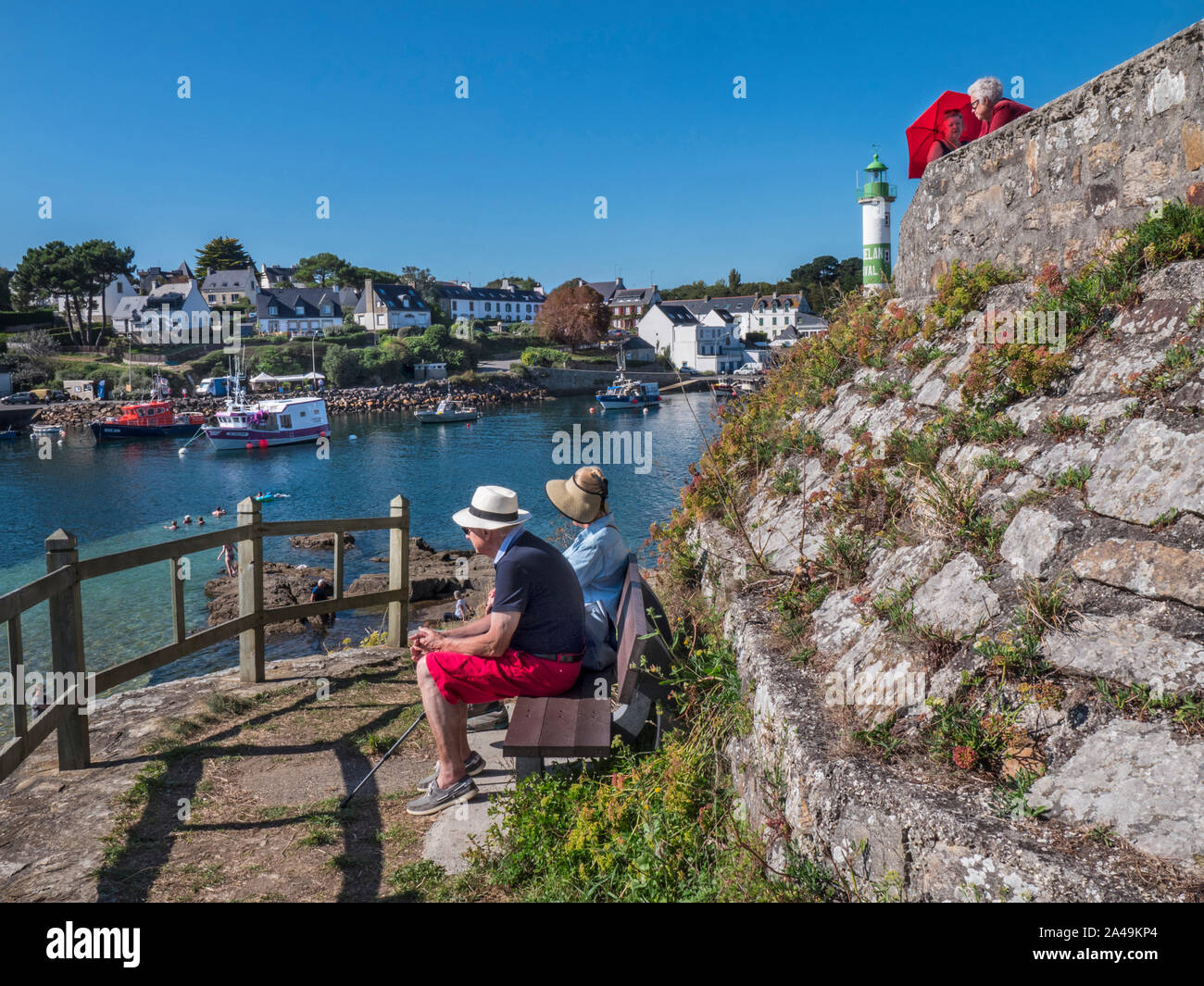 Les touristes DOELAN BRETAGNE SUN BANQUETTE FRANCE SUR MER port de pêche avec phare derrière Doelan, Moelan sur Mer, Finistère, Bretagne France Banque D'Images