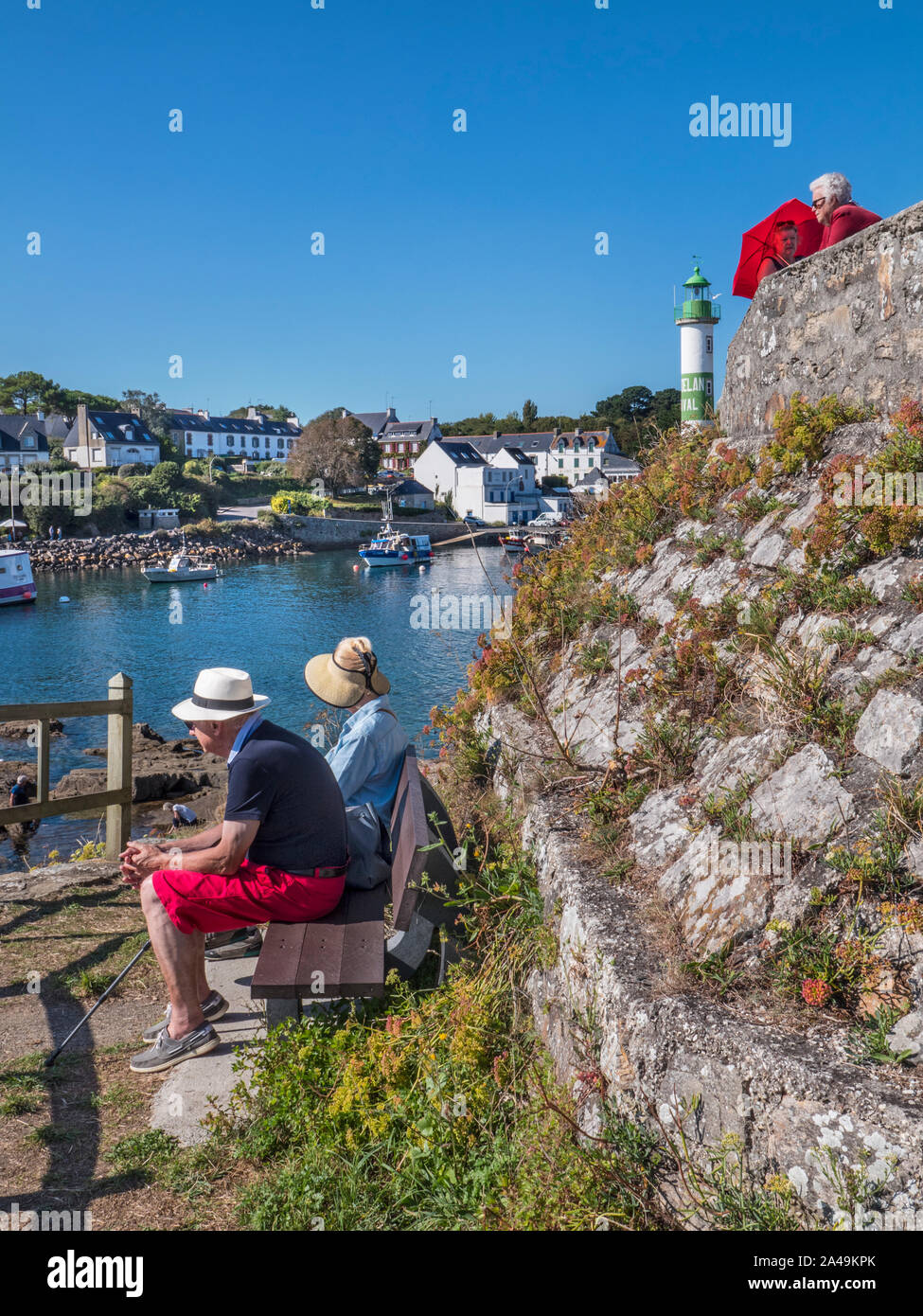Les touristes DOELAN BRETAGNE CHAPEAUX SOLEIL BANQUETTE FRANCE SUR MER port de pêche avec phare derrière Doelan, Moelan sur Mer, Finistère, Bretagne France Banque D'Images