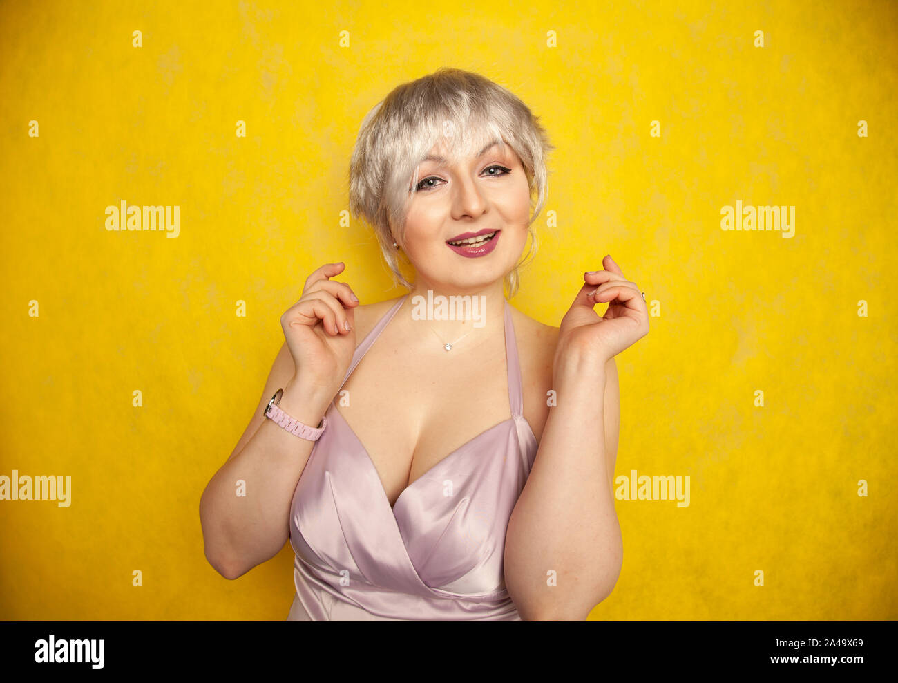 Heureux cheveux courts blonde avec grande taille corps posant en robe couleur lilas jaune sur fond studio seul Banque D'Images