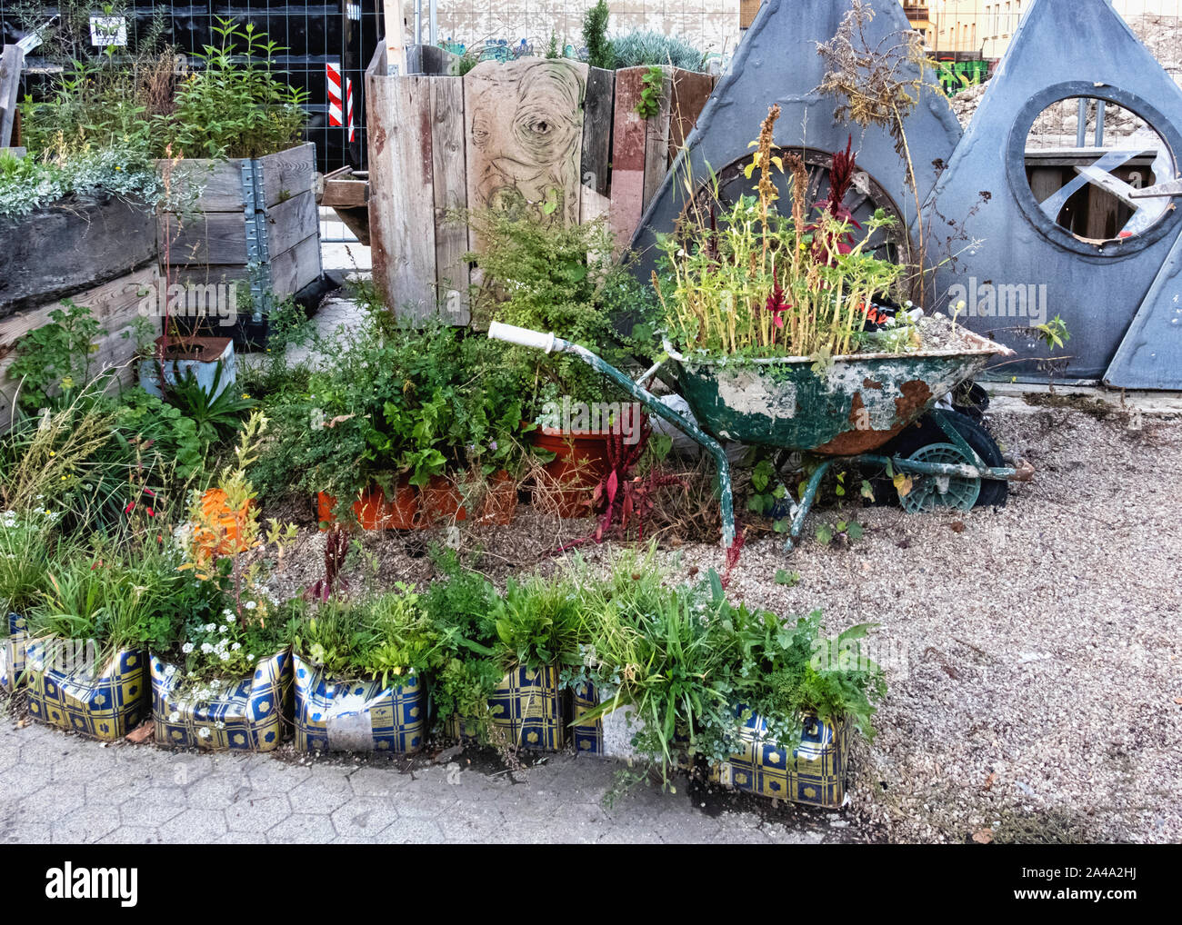 Vollguter jardin communautaire. Les plantes en contenants à l'aide de matériaux recyclés et la vieille brouette. Une piscine espace commun pour tous dans Neukölln, Berlin. Banque D'Images