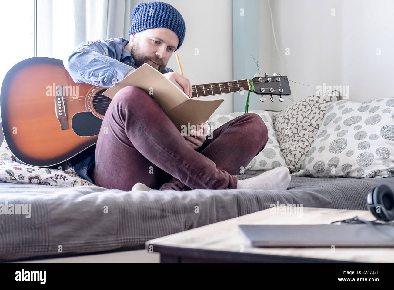 Jeune homme enthousiaste, compositeur de musique d'écrire dans son carnet et la tenue d'une guitare acoustique, assis sur un canapé, dans une maison confortable de l'environnem Banque D'Images