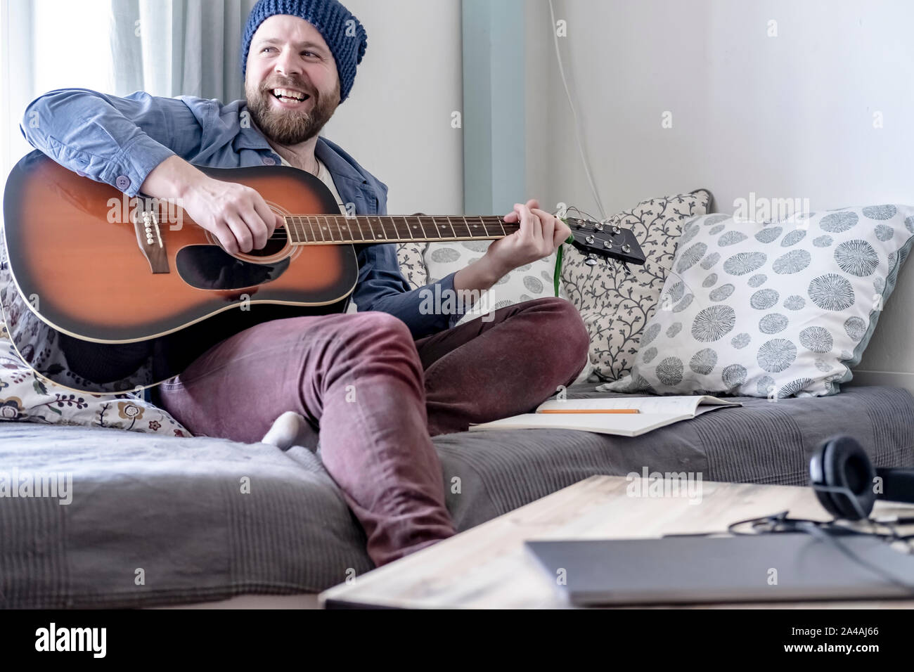 Jeune compositeur joue la musique écrite à la guitare acoustique, heureux du résultat, souriant joyeusement à ses amis, dans une maison confortable de l'environnem Banque D'Images
