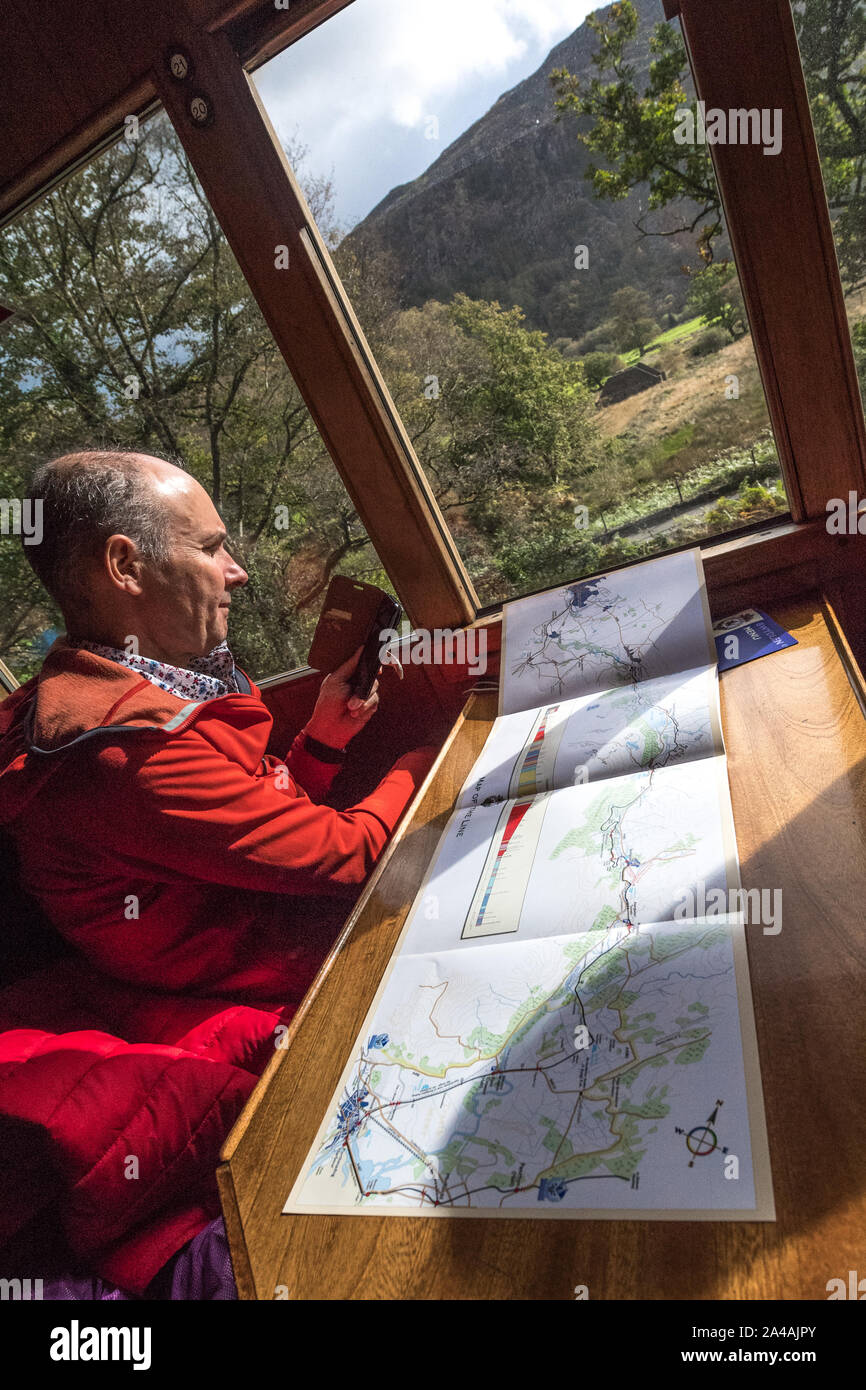 Photographier des passagers à l'aide d'un téléphone mobile à l'intérieur d'un entraîneur de rail sur le Ffestiniog & Welsh Highland Railway avec une carte de l'itinéraire du train sur la table Banque D'Images