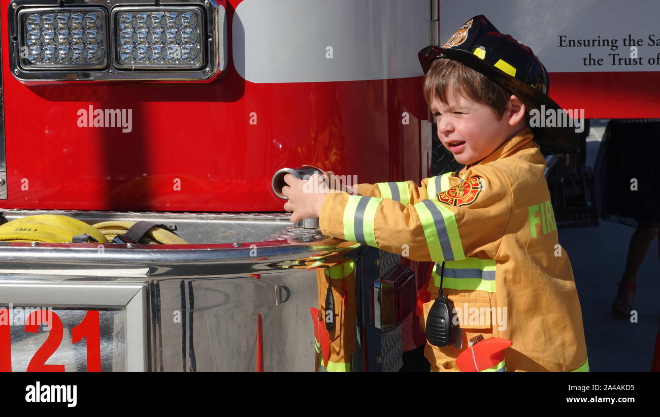 Un petit garçon habillé en pompier est heureux d'explorer un camion d'incendie à la station d'incendie portes ouvertes. Banque D'Images