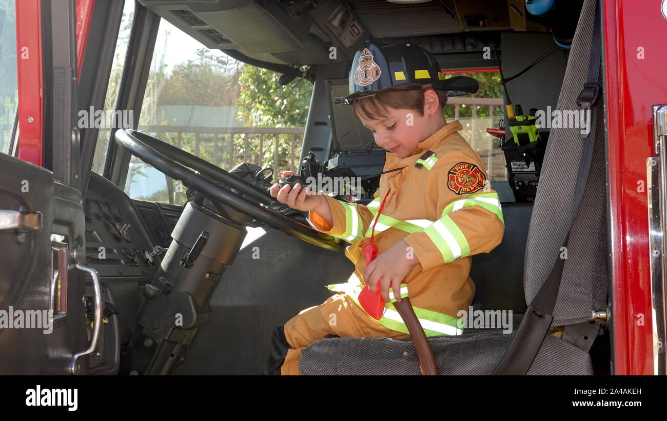 Un petit garçon habillé en pompier est heureux d'explorer un camion d'incendie à la station d'incendie portes ouvertes. Banque D'Images