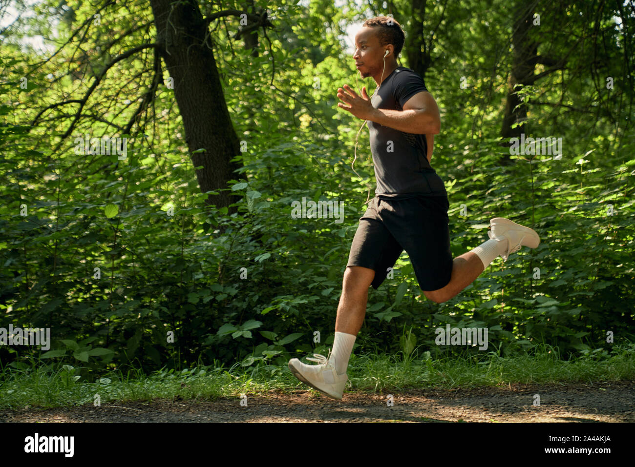 De jeunes africains dans la formation de canaux chauds en forêt matin ensoleillé. Sportsman exécutant marathon sur la passerelle du parc et l'écoute de la musique. Le port sportif en blanc les espadrilles et les chaussettes, t-shirt noir et un short. Banque D'Images De jeunes africains dans la formation de canaux chauds en forêt matin ensoleillé. Sportsman exécutant marathon sur la passerelle du parc et l'écoute de la musique. Le port sportif en blanc les espadrilles et les chaussettes, t-shirt noir et un short. Banque D'Images