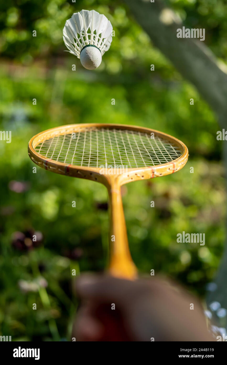 Une main tient une raquette de badminton et de lancer un volant, sur un fond vert, un jour d'été. Close-up. Banque D'Images