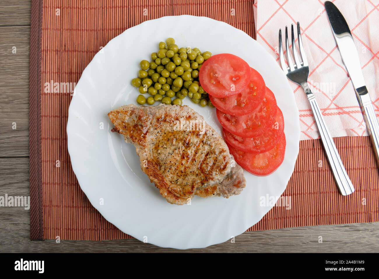 Hacher la viande steak de porc grillé avec des petits pois et les tomates. Vue d'en haut Banque D'Images