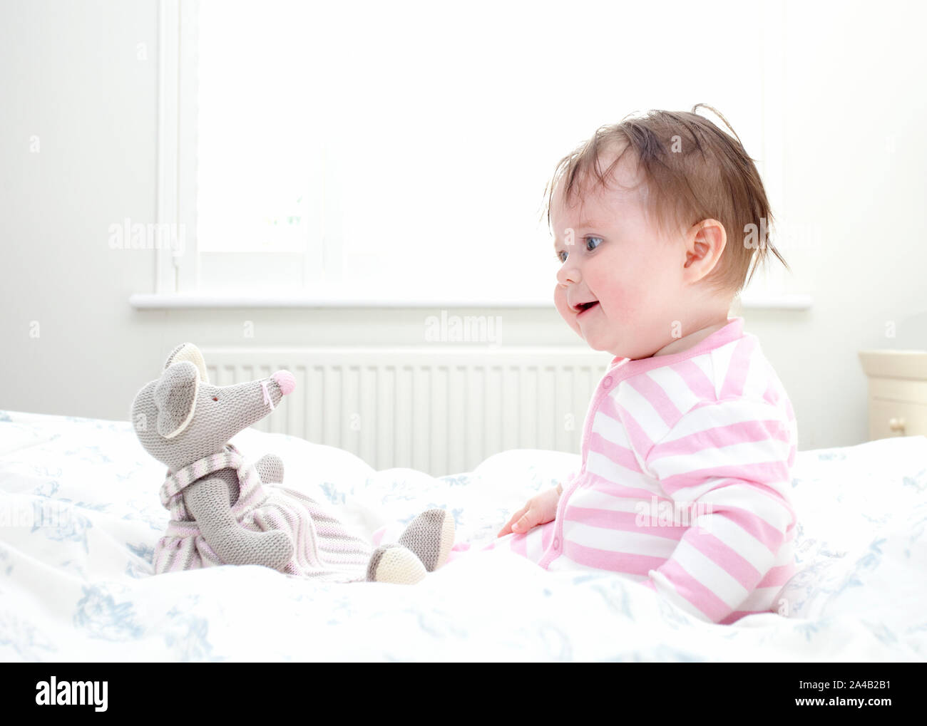 Bébé assis dans le lit jouant avec la souris jouet Banque D'Images