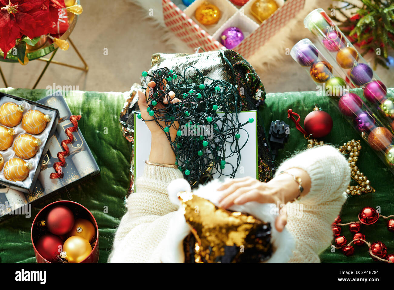 Saison de vacances. Vue de dessus de la mode femme malheureuse dans sparkle gold sequin santa hat assis sur le divan dans le salon moderne à Noël holding t Banque D'Images