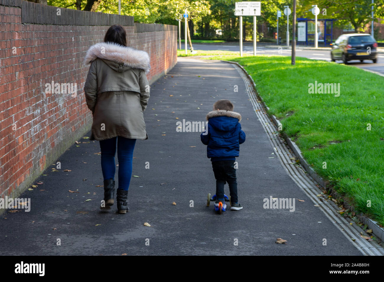 Une mère marche sur le trottoir avec son jeune fils de la trottinette à côté d'elle Banque D'Images