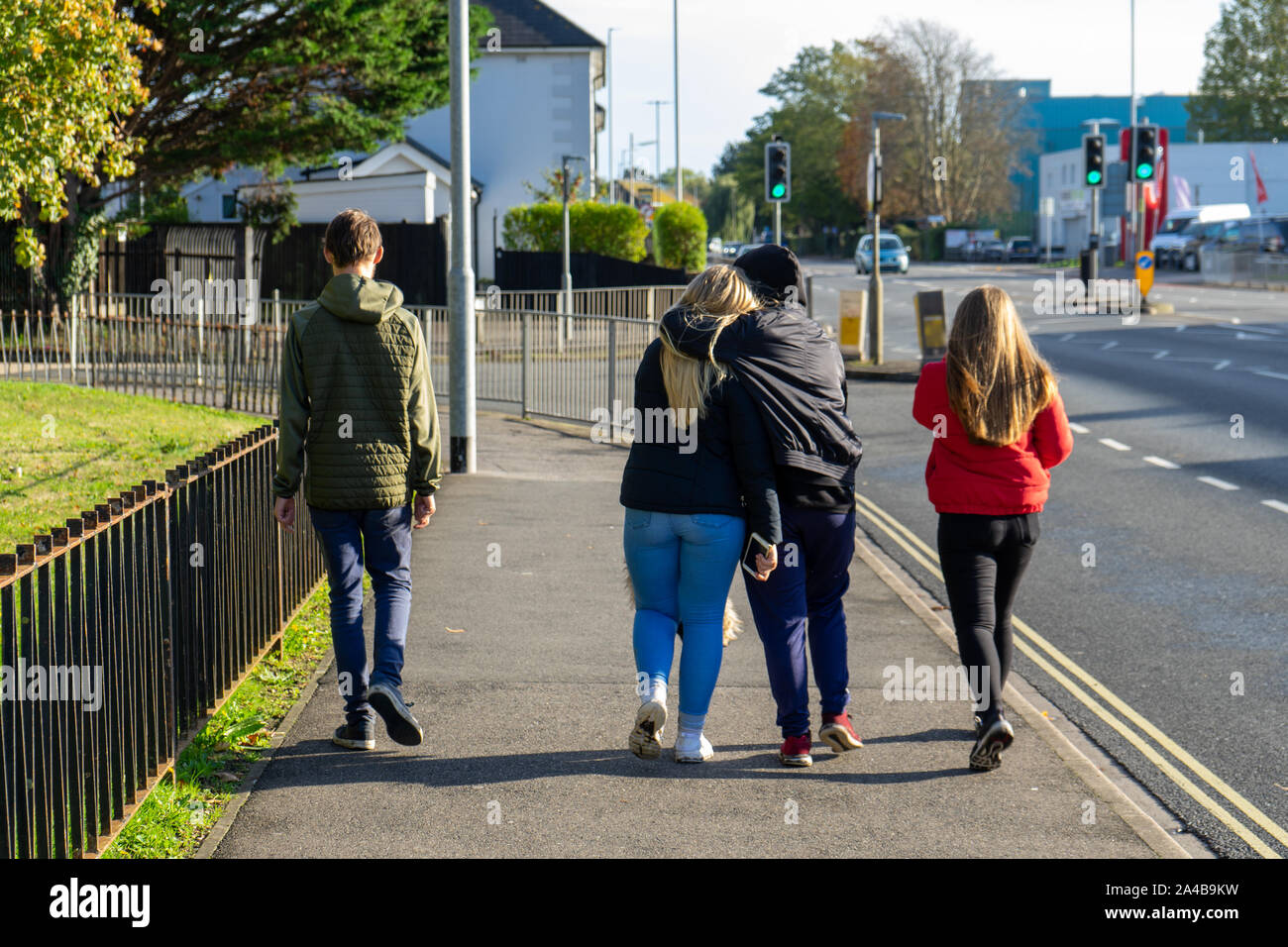 4 adolescents marcher dans une rue avec deux d'entre eux hugging Banque D'Images
