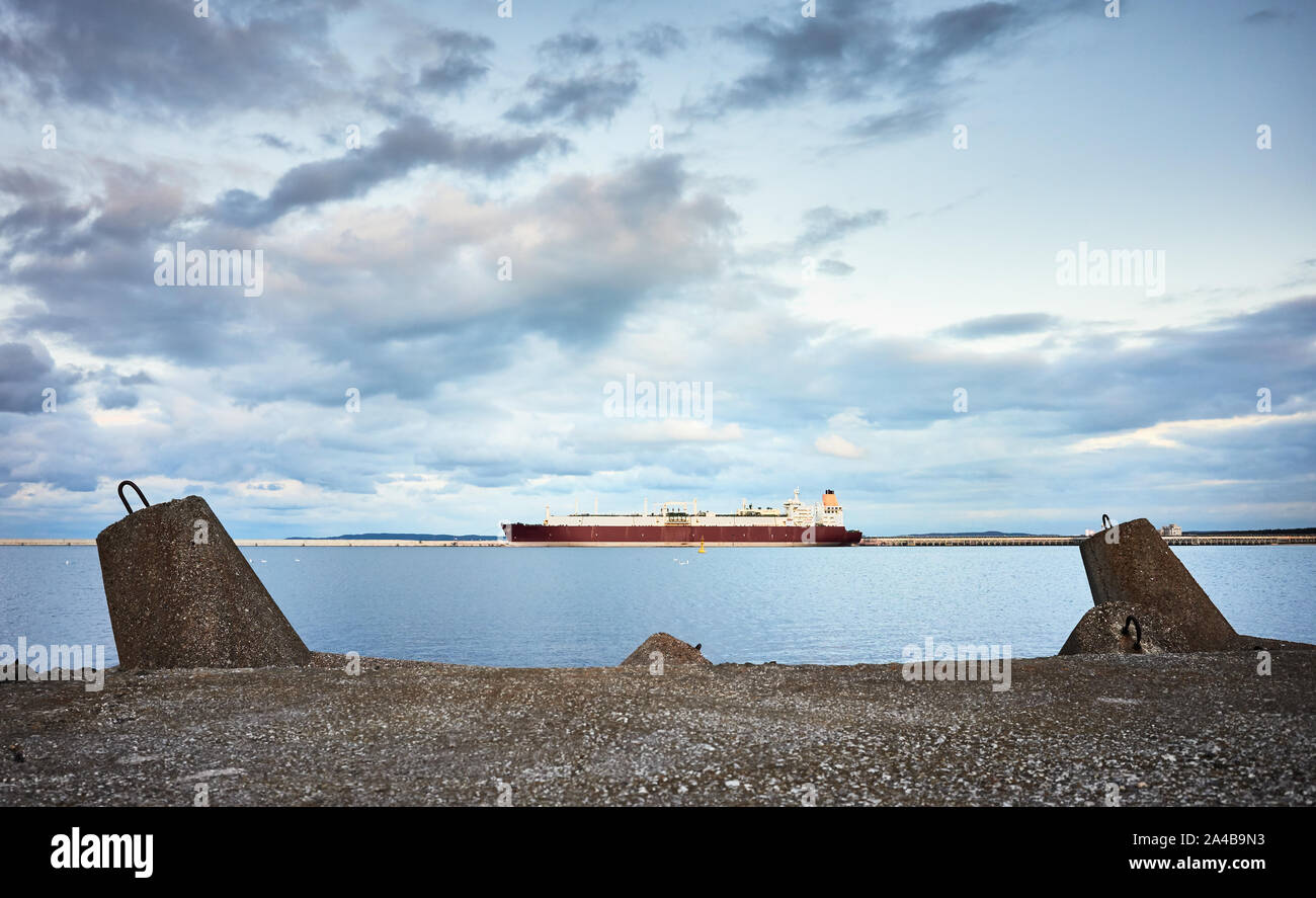 Brise-lames en béton avec un méthanier à distance au coucher du soleil. Banque D'Images