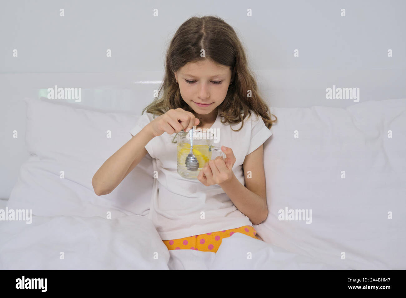 Smiling little girl holding un verre de boisson faite maison avec du citron en séance accueil linge de lit blanc. Banque D'Images