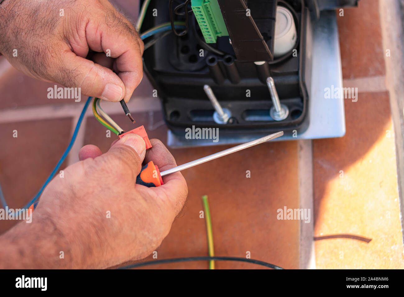 Mains d'un homme qui sont la connexion d'un câble à une bande d'alimentation électrique d'un moteur et d'un tournevis plat, avec le moteur électrique à l'arrière-plan Banque D'Images