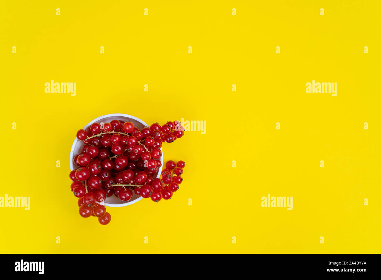 Un bol blanc de cassis avec quelques fruits sur une surface jaune Banque D'Images