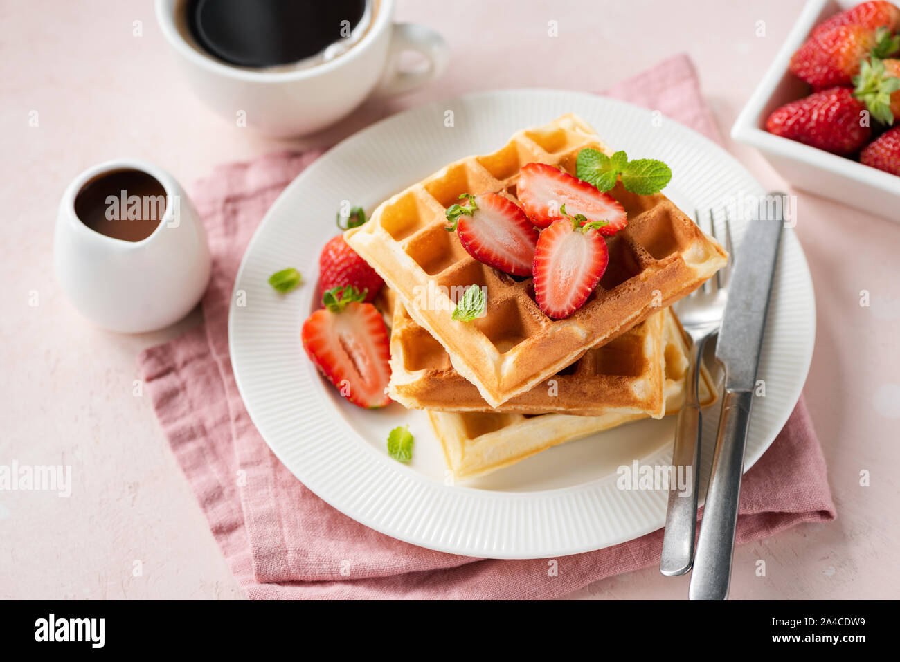 Square des gaufres belges avec des fraises servi avec une tasse de café noir et de sauce au chocolat sur fond rose Banque D'Images