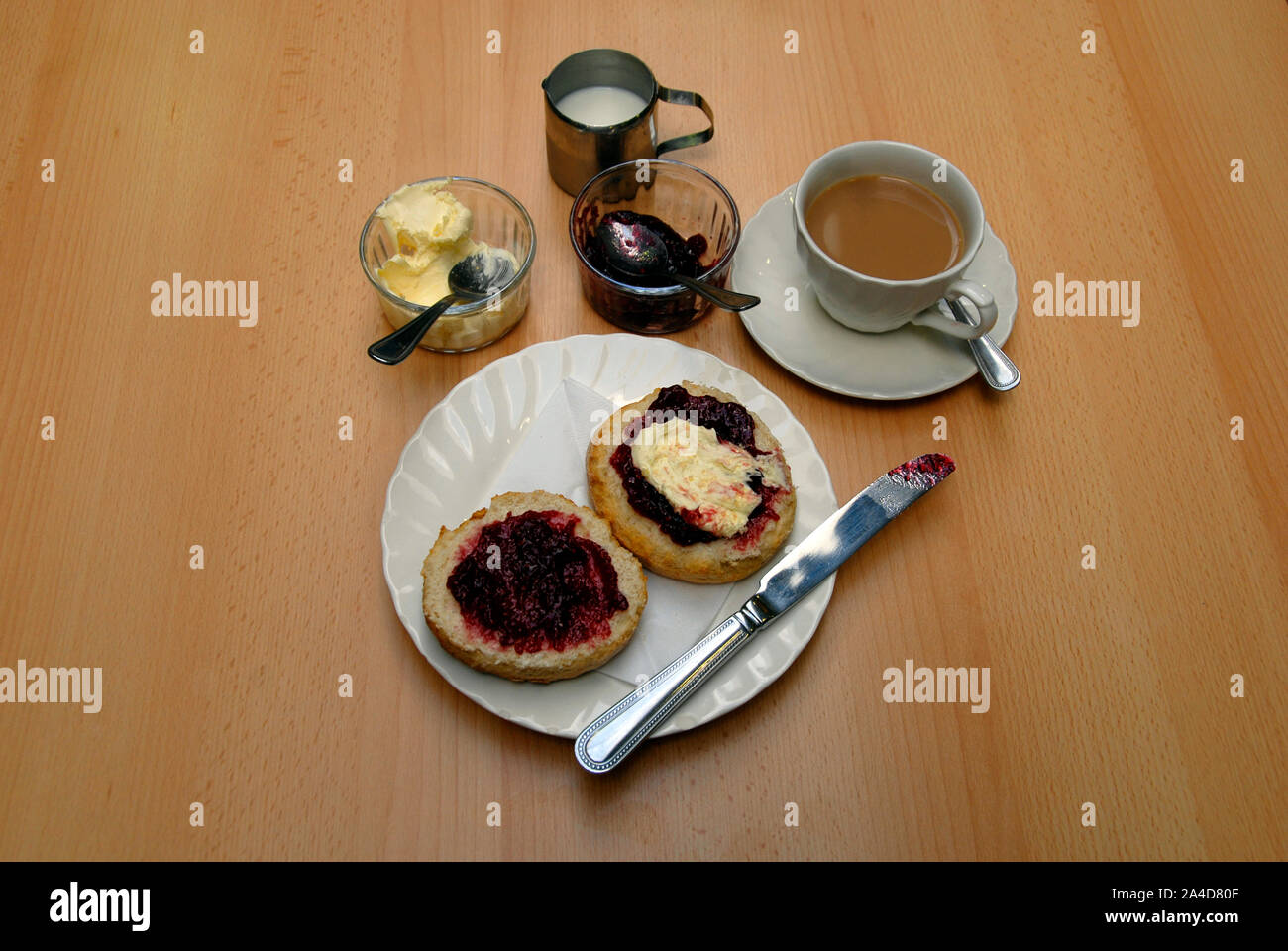 Un thé à la crème traditionnel avec grand scone coupé en deux, avec la confiture de framboises et de crème caillée sur une moitié et la confiture de framboises sur l'autre Banque D'Images