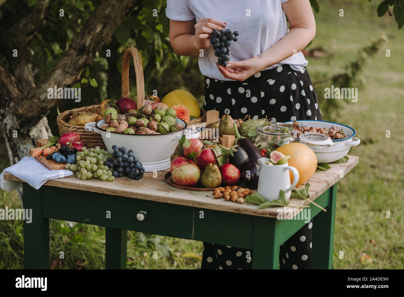 Femme debout par une table avec des fruits et légumes frais tenant une grappe de raisins, Serbie Banque D'Images