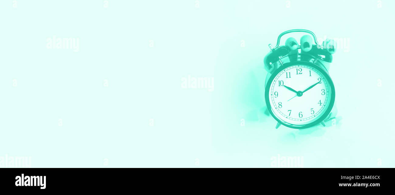 Réveil noir tenir la main à travers le trou dans l'arrière-plan couleur menthe. Service de concept d'alerte. Couleur turquoise et vert à la mode. La routine du matin. Banner Banque D'Images