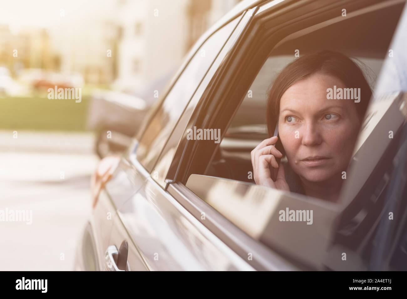 Businesswoman talking on mobile phone à l'intérieur de voiture de société alors qu'il était assis à l'arrière Banque D'Images