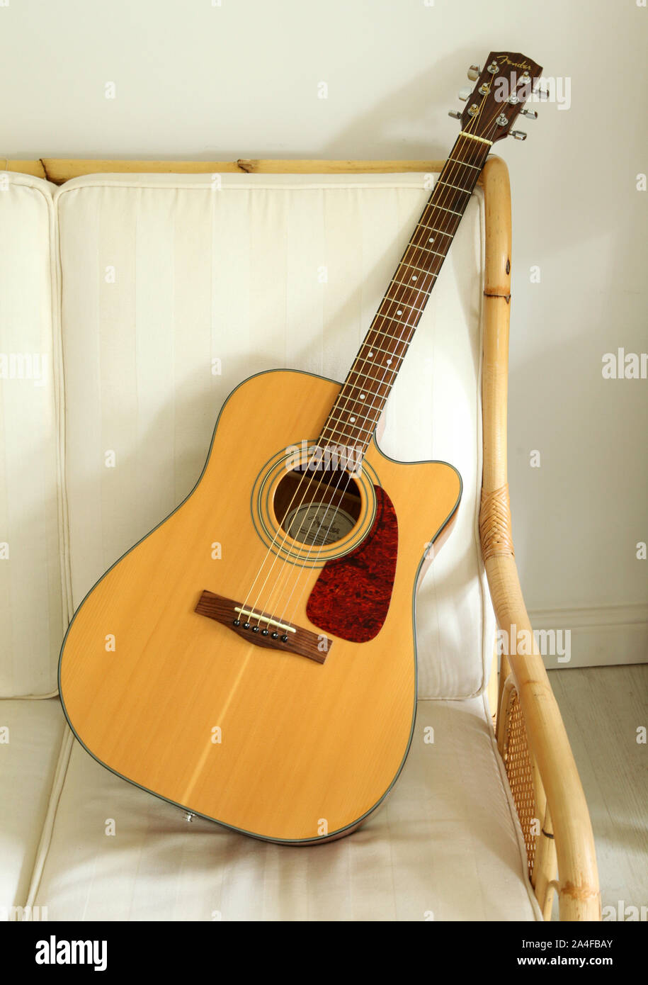 Une Fender guitare acoustique sur un canapé en rotin. Banque D'Images