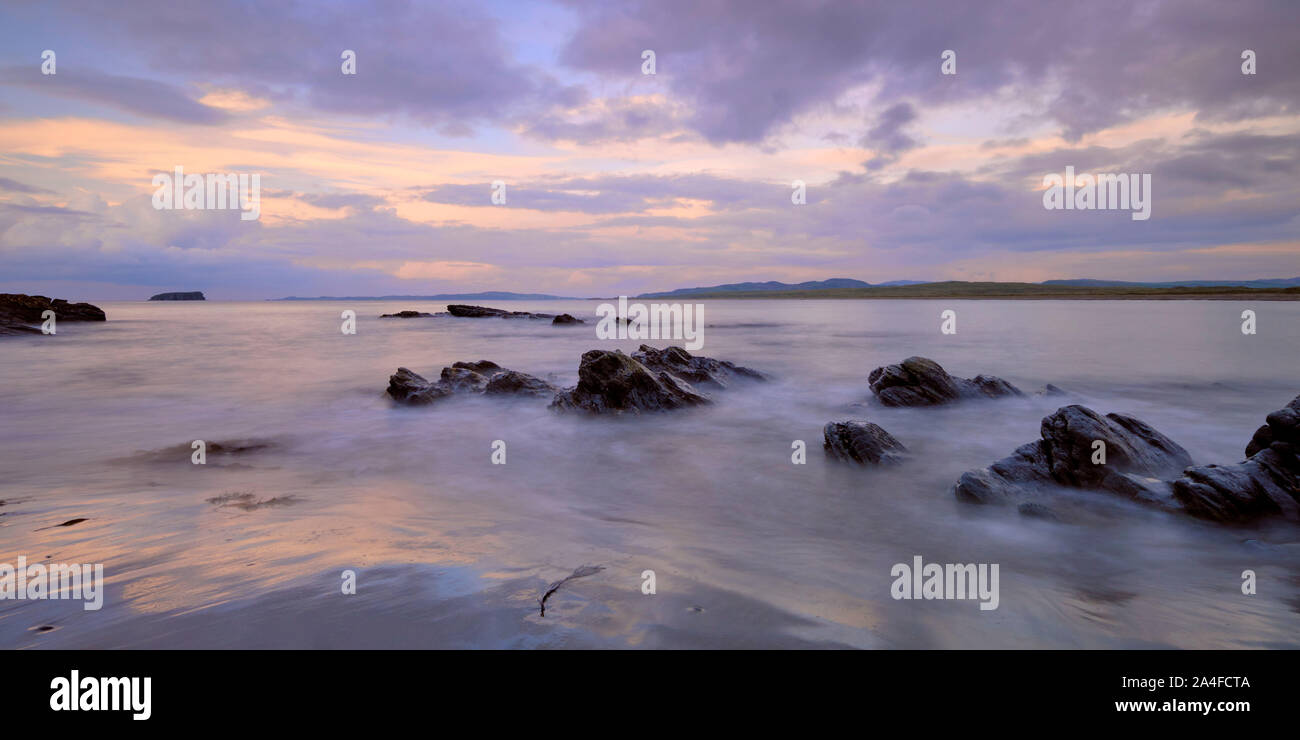 Coucher de soleil avec des nuages filandreux mauve sur Pollan Beach, Inishowen, Irlande. Les roches d'algues et de sable avec vue sur l'horizon sur la péninsule malin Banque D'Images