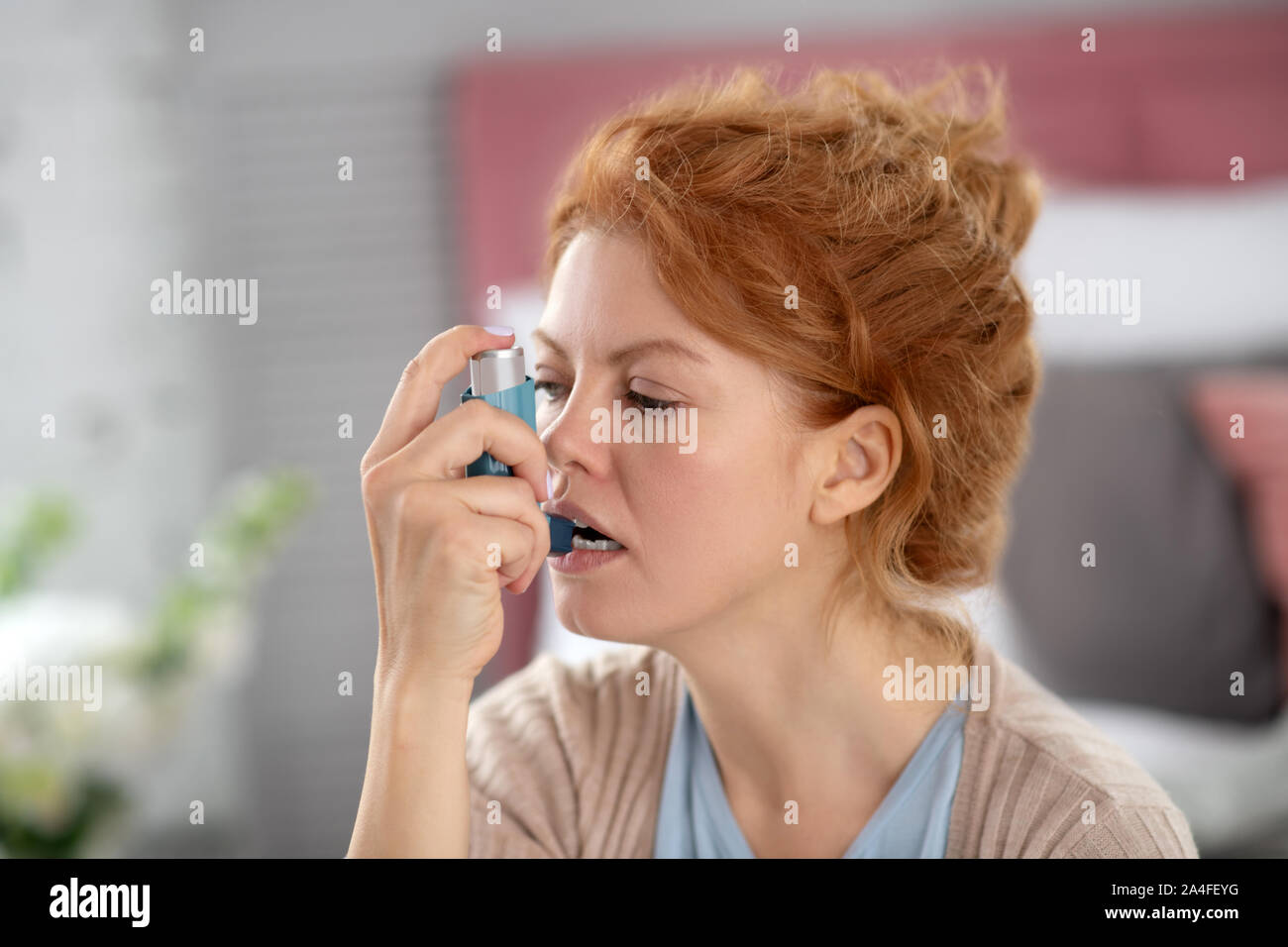 Red-haired woman ouvrant la bouche pendant l'utilisation d'inhalateur Banque D'Images